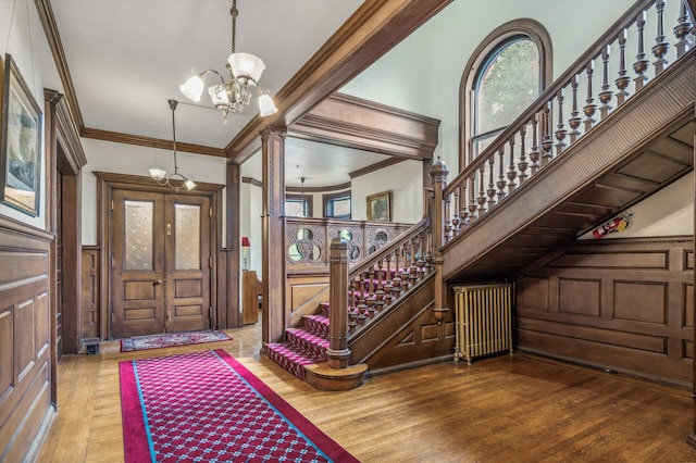 foyer with wood-type flooring, ornate columns, ornamental molding, and a notable chandelier