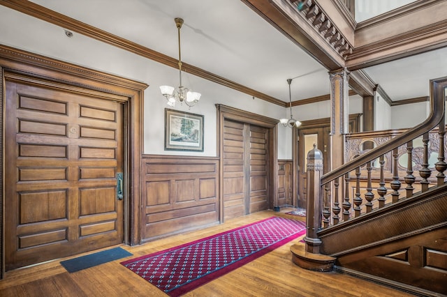 foyer with wooden walls, an inviting chandelier, ornamental molding, and hardwood / wood-style flooring