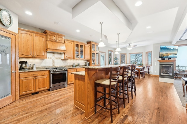 kitchen with light stone countertops, decorative light fixtures, stainless steel gas range oven, ceiling fan, and light hardwood / wood-style flooring