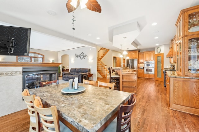 dining area featuring light wood-type flooring, ceiling fan, and a tile fireplace