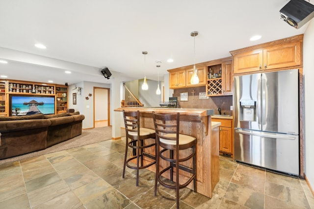 kitchen with stainless steel refrigerator with ice dispenser, sink, a breakfast bar area, and pendant lighting