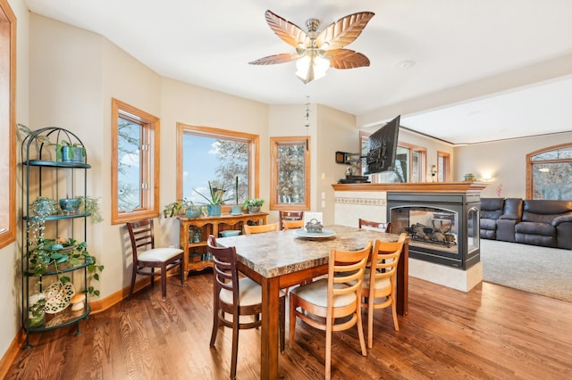 dining space featuring ceiling fan, a multi sided fireplace, and hardwood / wood-style floors