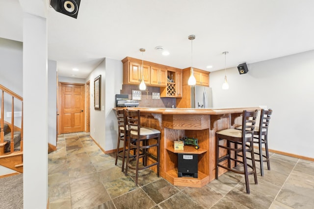 kitchen featuring kitchen peninsula, stainless steel refrigerator with ice dispenser, decorative backsplash, a kitchen breakfast bar, and hanging light fixtures