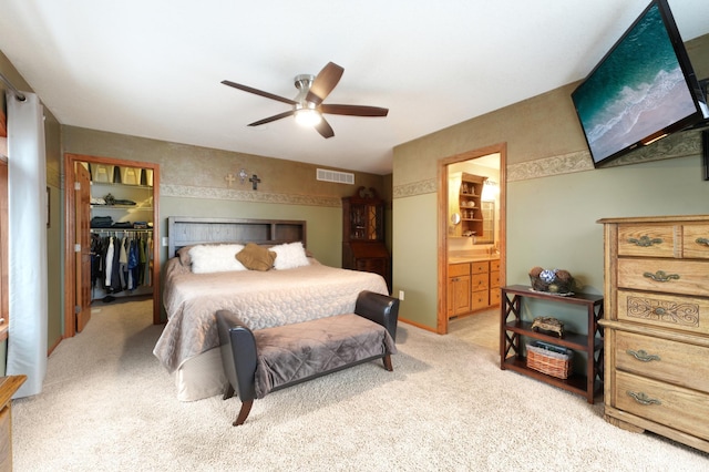 bedroom with light carpet, a spacious closet, ceiling fan, connected bathroom, and a closet