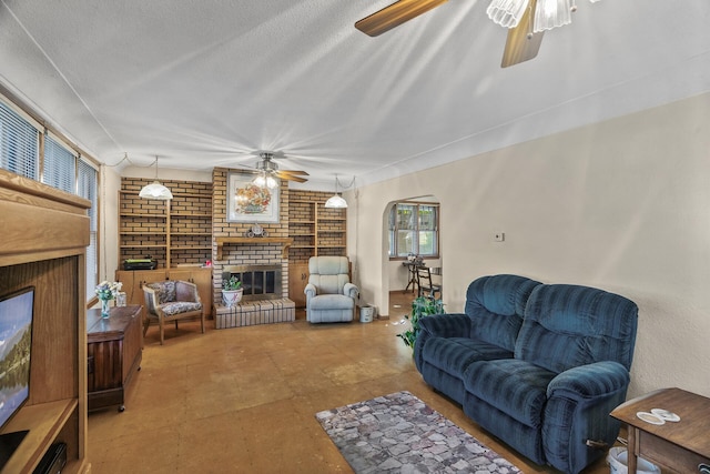 living room featuring a brick fireplace, a textured ceiling, and ceiling fan