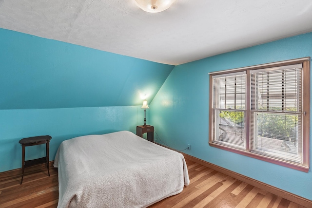 bedroom with hardwood / wood-style flooring, a textured ceiling, and vaulted ceiling