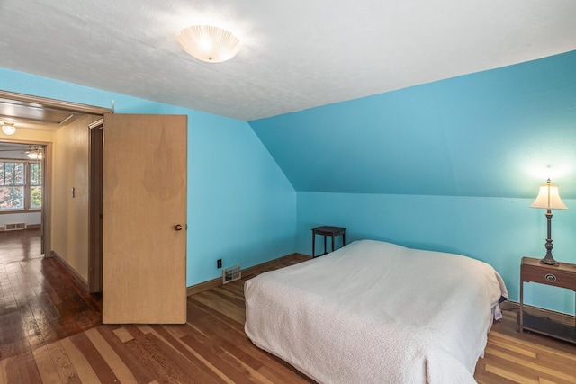 bedroom with dark hardwood / wood-style floors, a textured ceiling, and vaulted ceiling