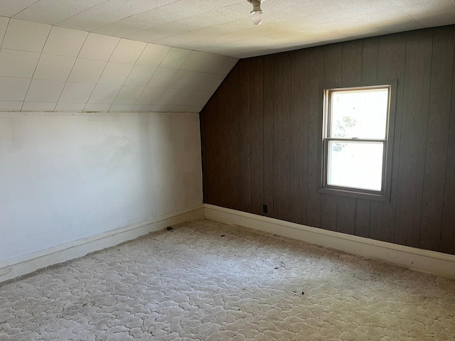 bonus room featuring light carpet, lofted ceiling, and wood walls