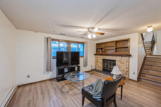 living room with a baseboard heating unit, a brick fireplace, light hardwood / wood-style floors, a textured ceiling, and ceiling fan