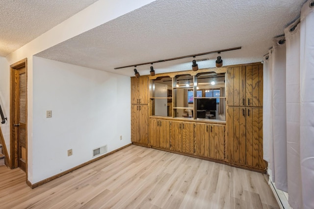 unfurnished living room with light wood-type flooring, a textured ceiling, and rail lighting