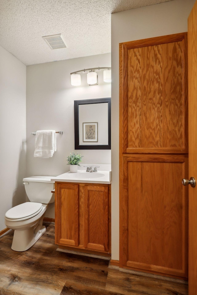 bathroom featuring a textured ceiling, wood-type flooring, vanity, and toilet