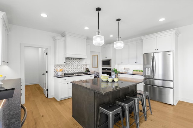 kitchen featuring white cabinets, a kitchen island, decorative light fixtures, light hardwood / wood-style flooring, and appliances with stainless steel finishes