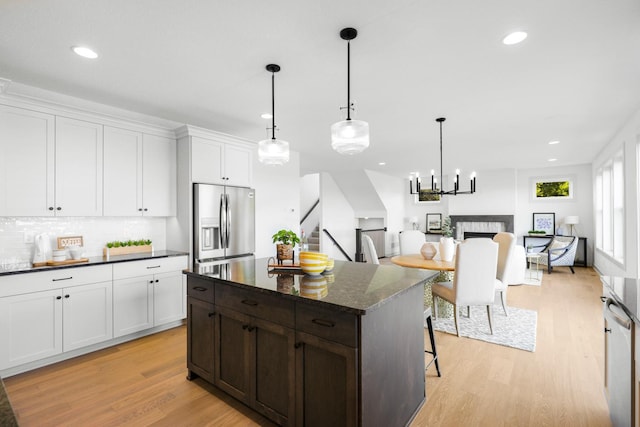 kitchen featuring a tile fireplace, a kitchen island, light wood-type flooring, dark stone counters, and stainless steel fridge with ice dispenser