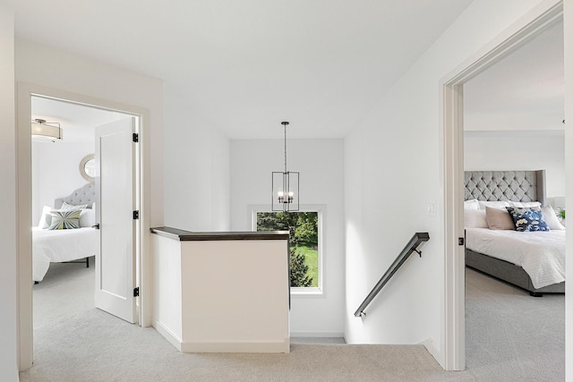 hallway with a notable chandelier and light colored carpet