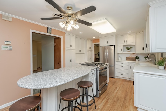 kitchen with sink, white cabinets, a kitchen bar, stainless steel appliances, and ceiling fan