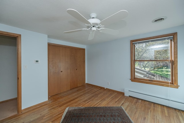 unfurnished bedroom with baseboard heating, ceiling fan, a closet, and light hardwood / wood-style flooring