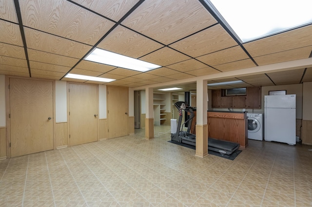 basement featuring a paneled ceiling, washer / clothes dryer, wooden walls, and white fridge