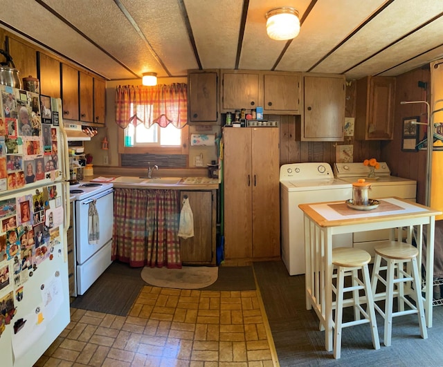 kitchen with a textured ceiling, white appliances, wooden walls, sink, and washer and dryer