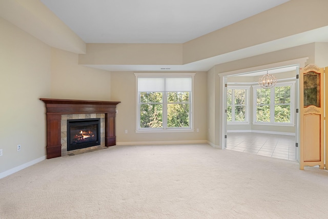 unfurnished living room with a notable chandelier, a tile fireplace, plenty of natural light, and light carpet