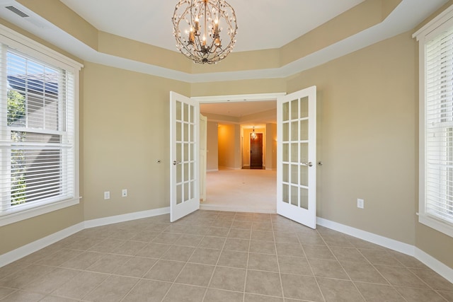 tiled spare room featuring a notable chandelier, a raised ceiling, french doors, and a wealth of natural light