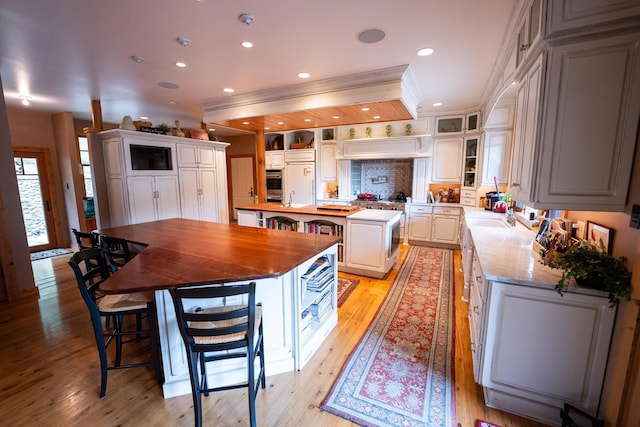 kitchen featuring white cabinetry, wooden counters, light wood-type flooring, a center island, and sink