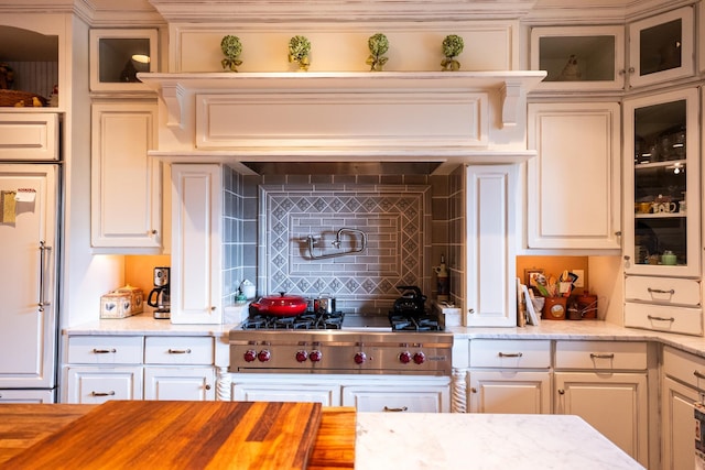 kitchen featuring tasteful backsplash, high end fridge, white cabinetry, stainless steel gas stovetop, and wood counters