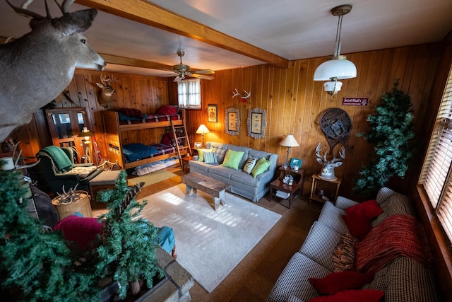 living room featuring ceiling fan, beamed ceiling, wooden walls, and a fireplace