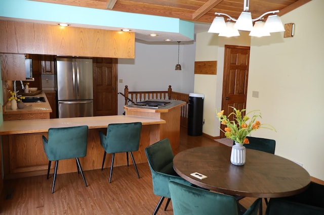 kitchen with kitchen peninsula, stainless steel fridge, beam ceiling, and hanging light fixtures