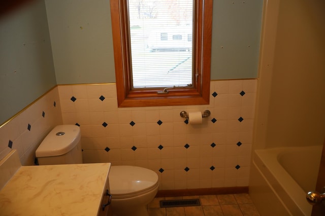 bathroom featuring tile walls, toilet, a bath, vanity, and tile patterned flooring