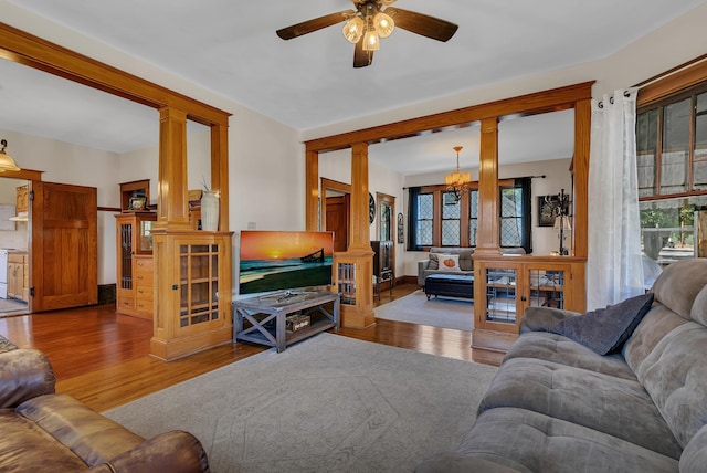 living room featuring ceiling fan with notable chandelier, wood-type flooring, and decorative columns