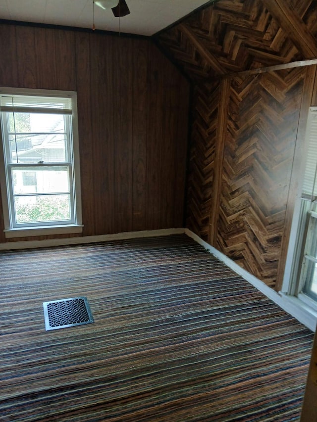 unfurnished room with ceiling fan, vaulted ceiling, and wooden walls