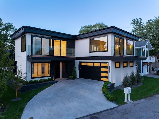 contemporary home featuring a garage, a balcony, a front yard, stucco siding, and driveway
