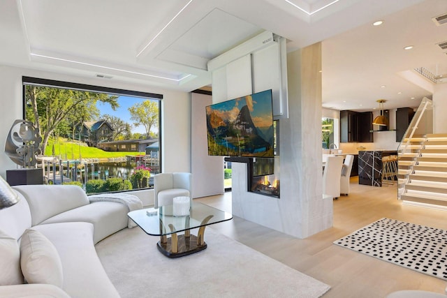 living area with a glass covered fireplace, recessed lighting, light wood finished floors, and visible vents