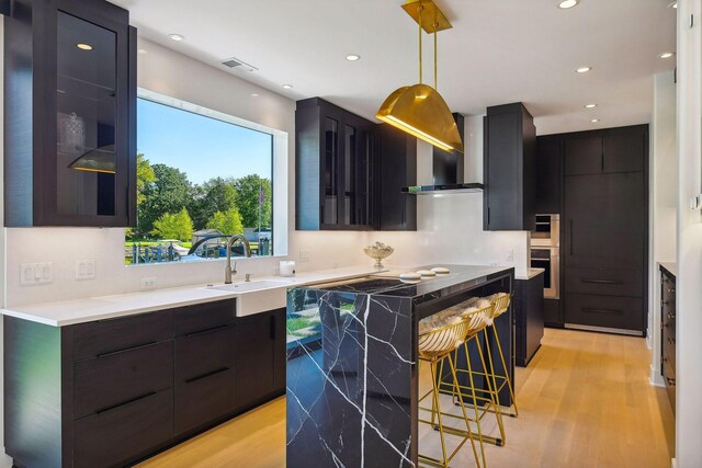 kitchen featuring a kitchen island, dark cabinets, hanging light fixtures, modern cabinets, and light wood-style floors