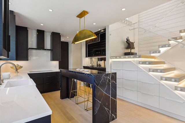 kitchen with wall chimney range hood, modern cabinets, a sink, light wood finished floors, and dark cabinets