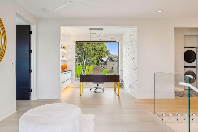 office area featuring baseboards, stacked washer and clothes dryer, and wood finished floors