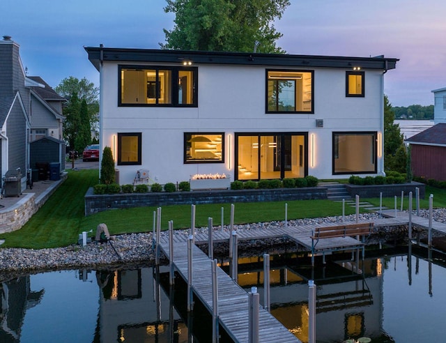 back of house at dusk featuring stucco siding and a yard