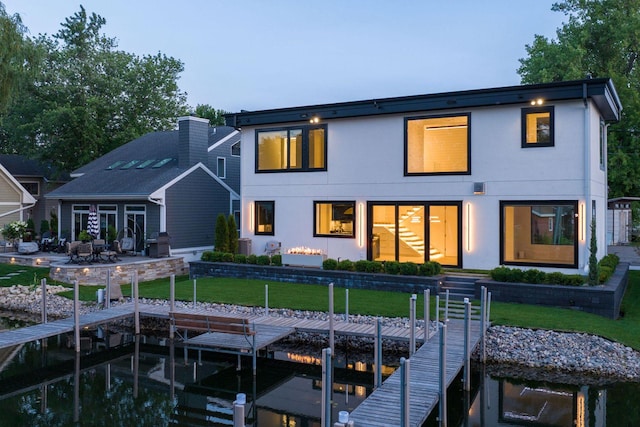 rear view of house featuring boat lift, stucco siding, a yard, and a patio