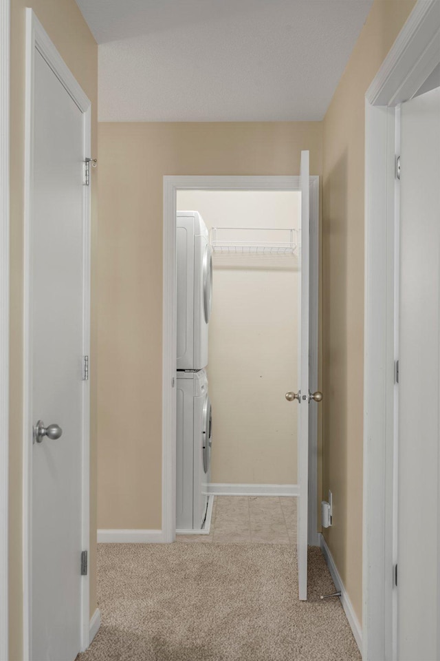 hall featuring stacked washer and dryer, carpet flooring, and baseboards