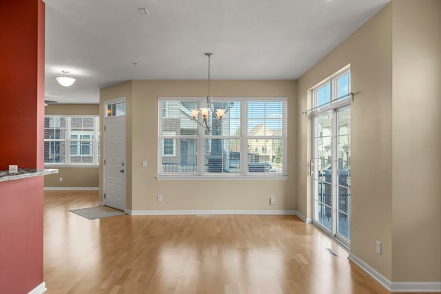 unfurnished dining area featuring a chandelier, light wood-style floors, baseboards, and visible vents