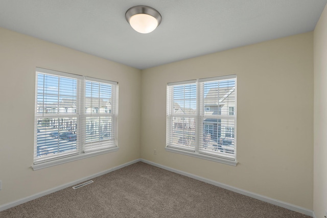 spare room featuring carpet flooring, visible vents, baseboards, and a healthy amount of sunlight