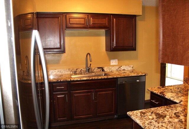 kitchen with appliances with stainless steel finishes, dark hardwood / wood-style flooring, light stone counters, dark brown cabinetry, and sink