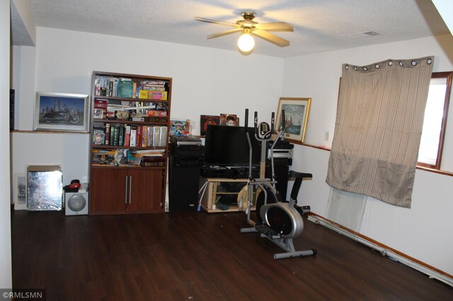 workout area with a textured ceiling, ceiling fan, and dark wood-type flooring