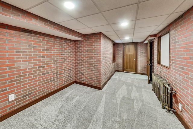 basement featuring light carpet, brick wall, and a paneled ceiling