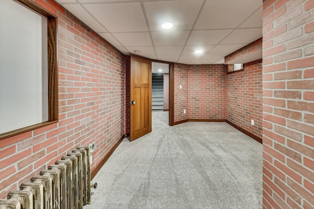 basement with light carpet, radiator, brick wall, and a drop ceiling