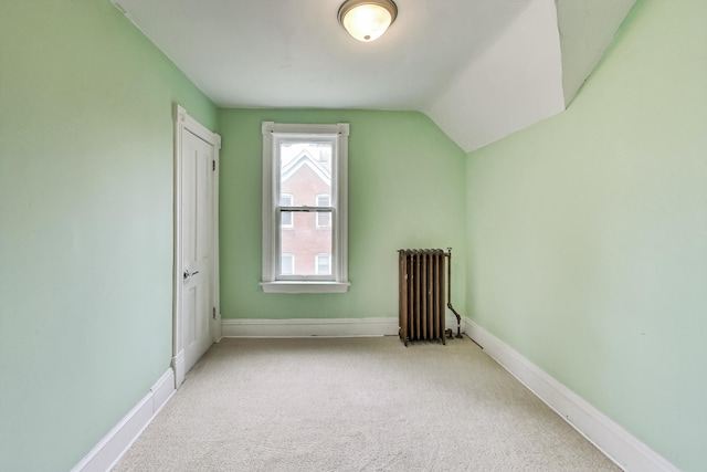 additional living space with radiator, light colored carpet, and vaulted ceiling