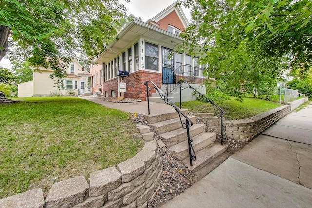 view of front of home with a sunroom, brick siding, and a front lawn