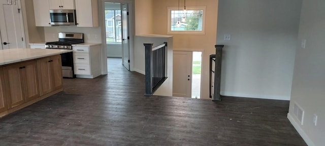 kitchen with stainless steel appliances, white cabinetry, dark wood-type flooring, and decorative light fixtures