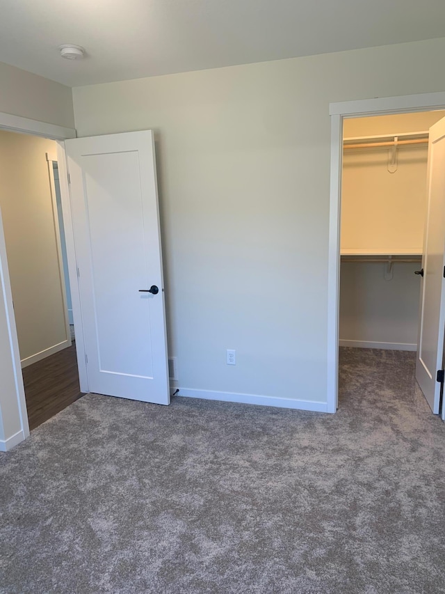 unfurnished bedroom with a spacious closet, dark carpet, and a closet