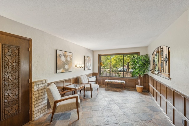 living area featuring a textured wall, a textured ceiling, and wainscoting